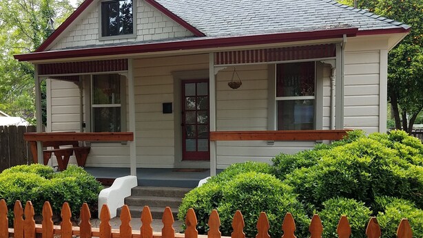 Una casa a un piano con tetto a due falde, un portico e un piccolo giardino anteriore con una recinzione in legno.