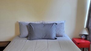 Un letto con biancheria bianca, due cuscini, un comodino rosso con una lampada e una coppia di asciugamani piegati sul letto.