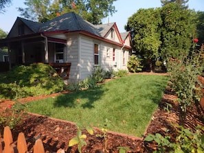 A residential house with a well-maintained lawn, a wooden deck, and a garden with various plants.