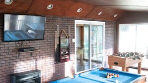 A pool table with billiard balls, a foosball table, a television mounted on a brick wall, and a fireplace. - Perfect Getaway In The Poconos! (House #1) HotTub !! Gameroom!! WiFi !! (Albrightsville)