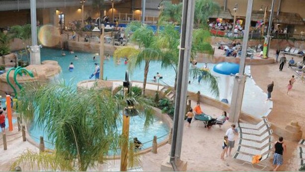 An indoor water park with multiple pools, slides, and a sandy area with lounge chairs. - Perfect Getaway In The Poconos! (House #1) HotTub !! Gameroom!! WiFi !! (Albrightsville)