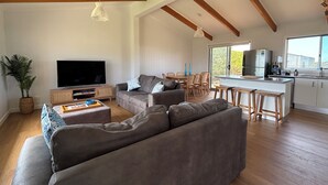 Un salon spacieux avec un grand canapé gris, un téléviseur à écran plat et un coin repas comprenant des chaises en bois et une table blanche.