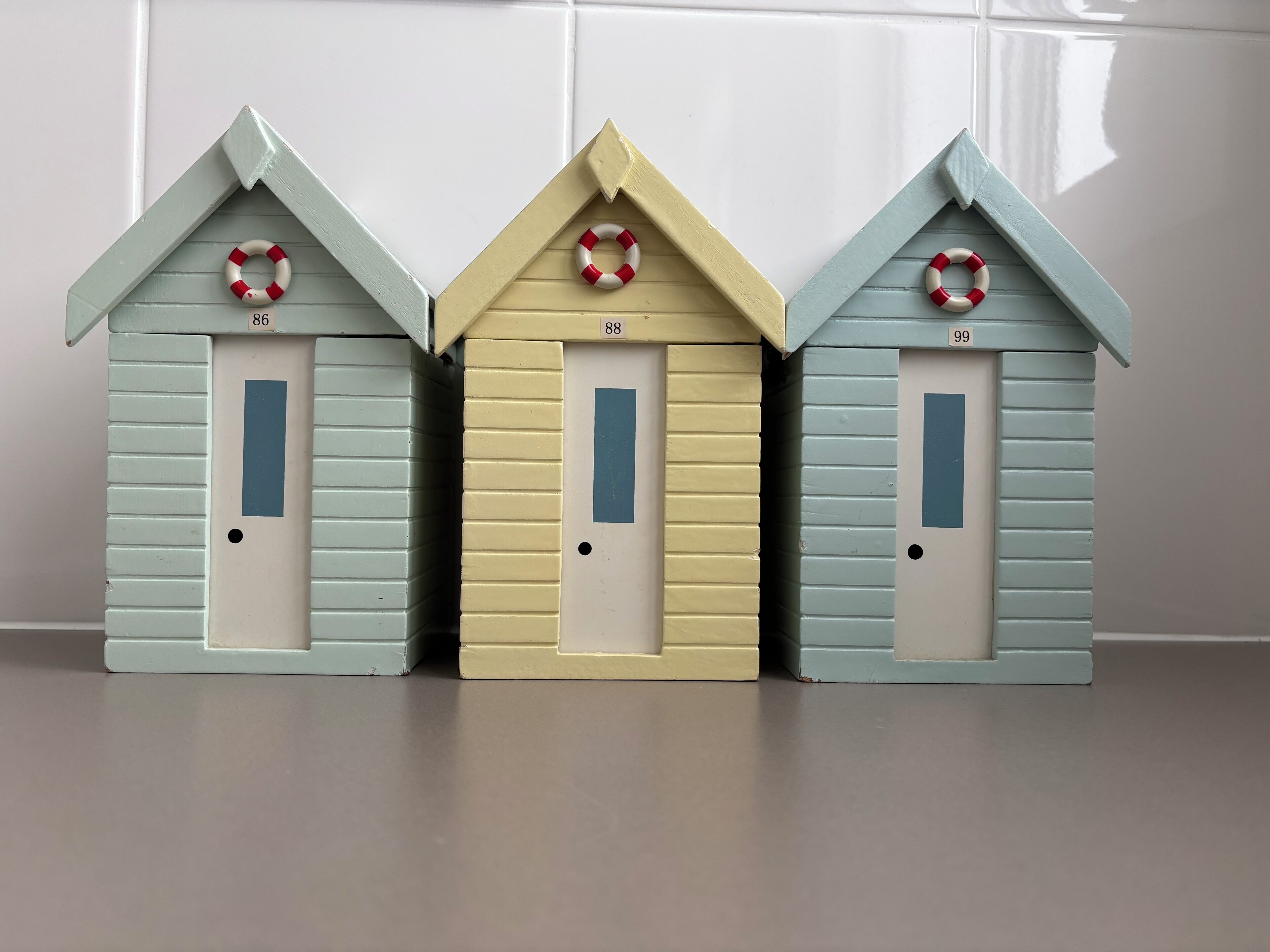 Three small, colorful houses with numbered doors and lifebuoys on the roofs.