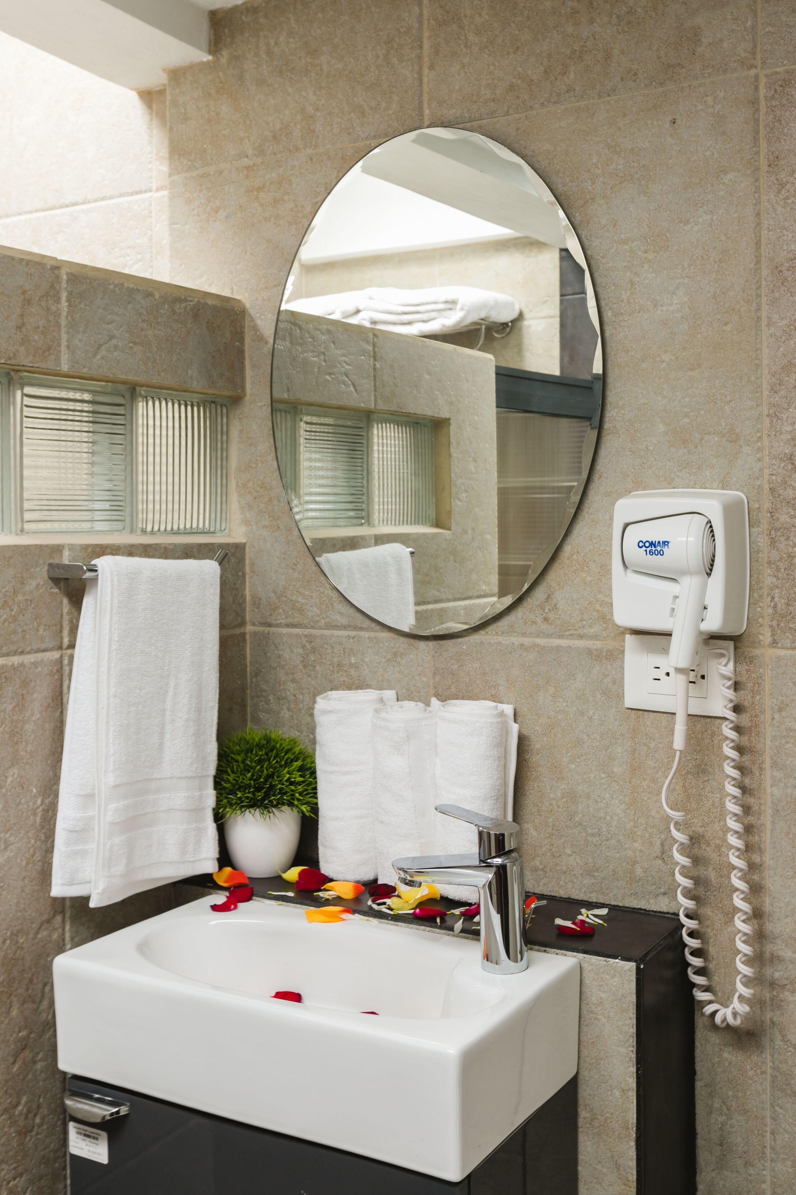 Un bagno con lavandino bianco, uno specchio, un asciugacapelli e asciugamani su un porta asciugamani.