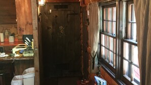 Interior rústico de una cabaña con detalles de madera, una mesa de comedor con una vela y una ventana con cortinas.