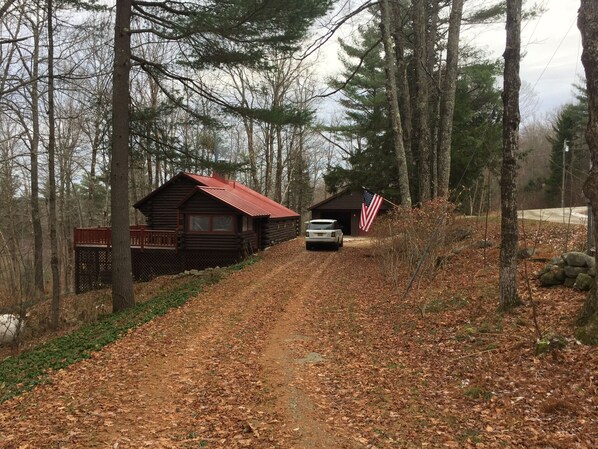 Una baita dal tetto rosso e un'asta con la bandiera americana, immersa tra alberi e un sentiero sterrato.