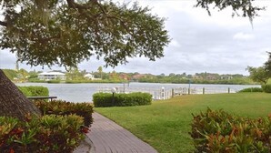Ein gepflasterter Weg führt zu einer Uferpromenade mit Blick auf einen See und Häuser im Hintergrund.