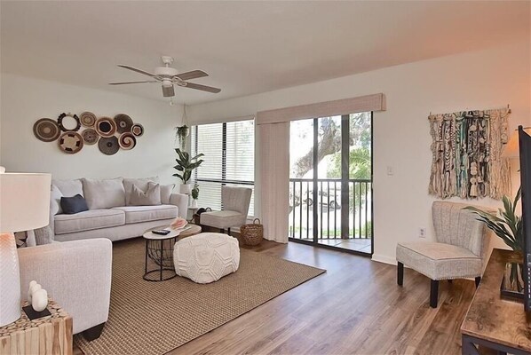 A spacious living room with a grey sofa, a coffee table, and a ceiling fan. - Newly Refurnished Tropical Townhouse - Watch Dolphin in the Bay, Fish from the Docks! Unit B62 (Siesta Key)