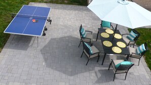 Een terras buiten met een tafeltennis tafel, stoelen en een tafel met een witte parasol.