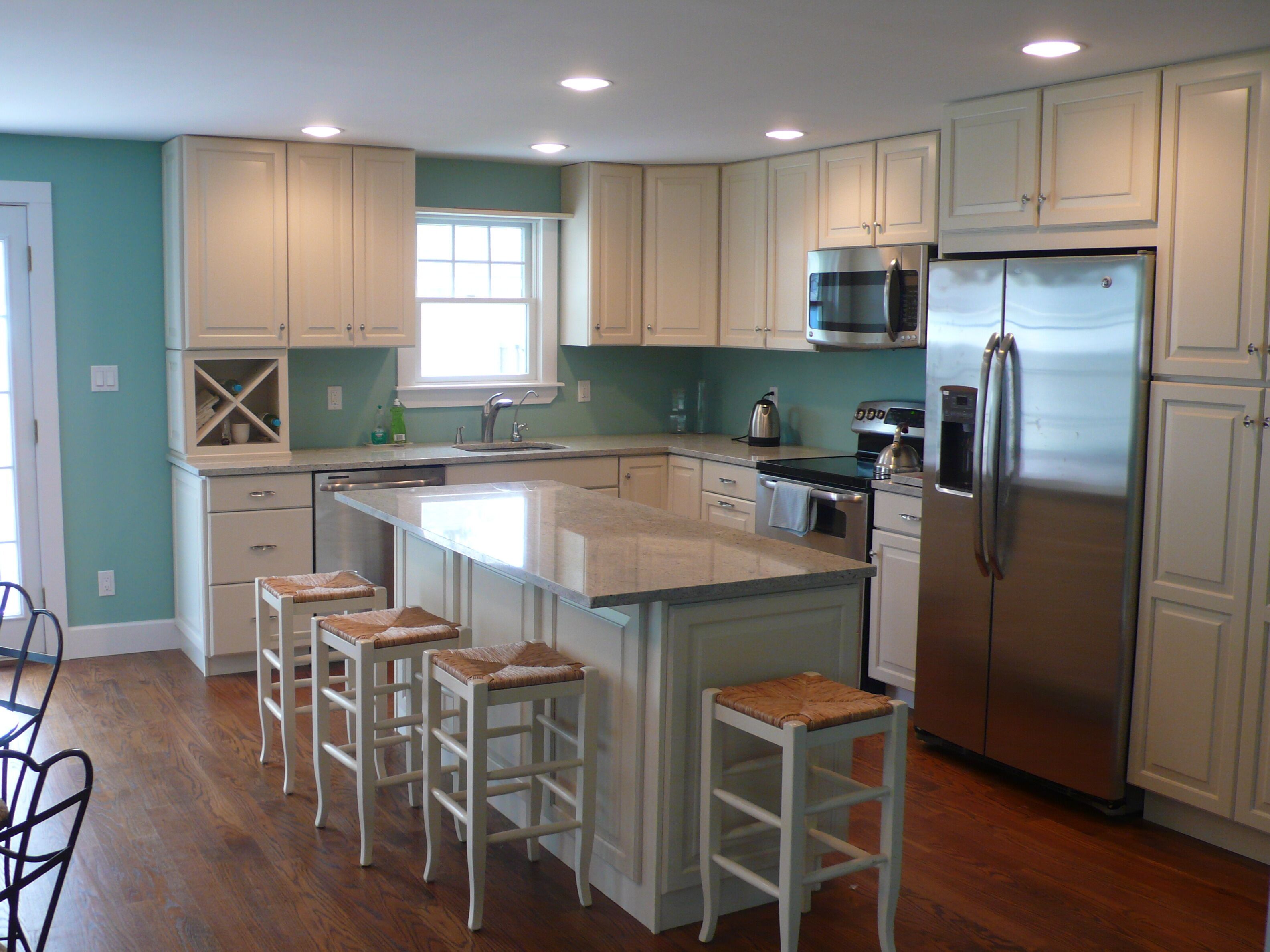 A kitchen with a central island, bar stools, a stainless steel refrigerator, and white cabinetry.