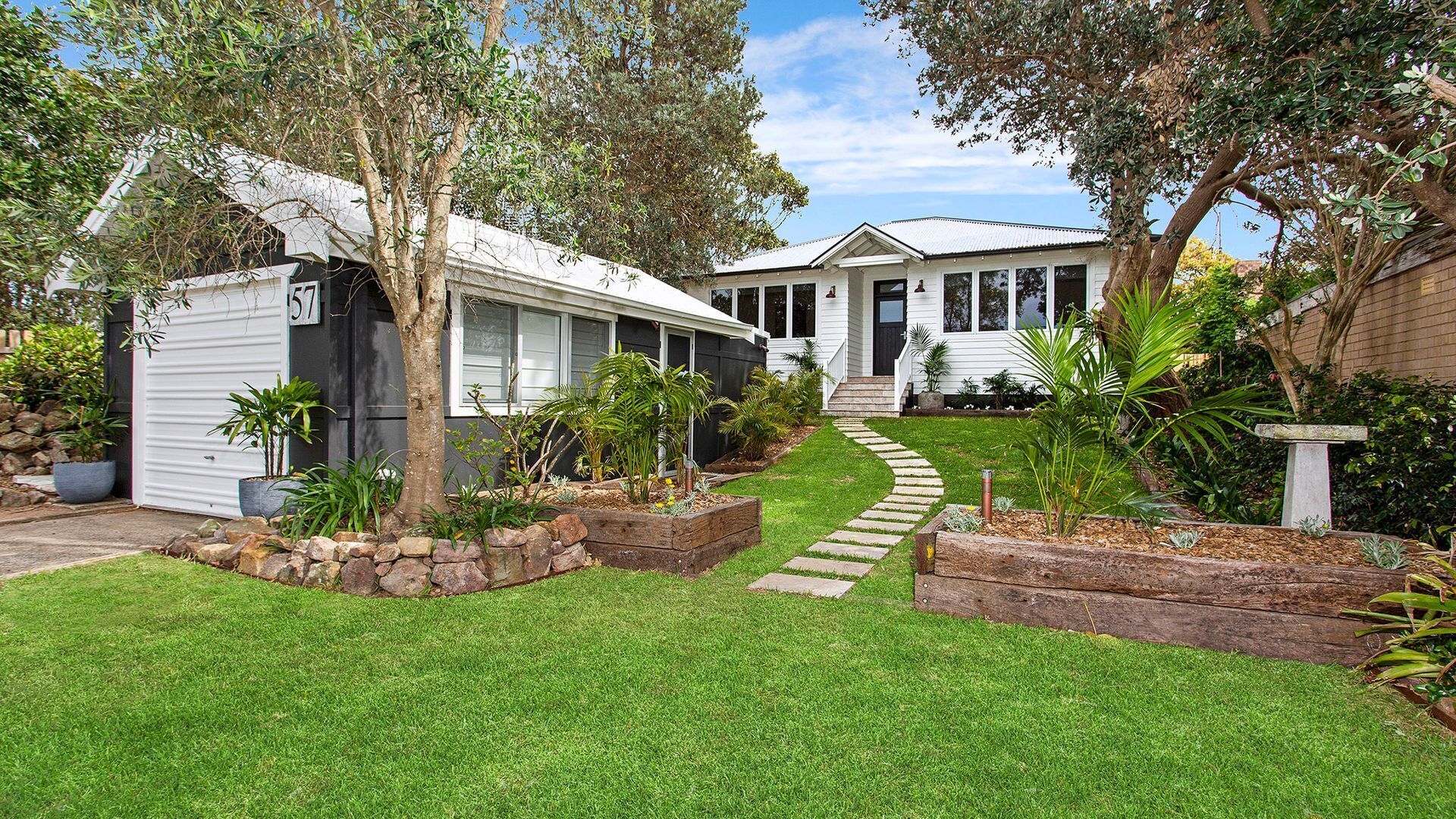 A residential property with a well-maintained lawn, a stone pathway leading to the house, and a variety of plants and trees.