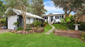 A residential property with a well-maintained lawn, a stone pathway leading to the house, and a variety of plants and trees. - Saltwater - walk to the beach (Werri Beach)