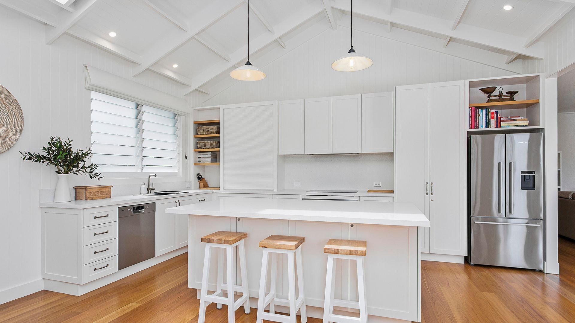 A modern kitchen with white cabinetry, a stainless steel refrigerator, and a large island with bar stools.