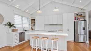 A modern kitchen with white cabinetry, a stainless steel refrigerator, and a large island with bar stools. - Saltwater - walk to the beach (Werri Beach)