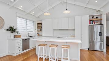 A modern kitchen with white cabinetry, a stainless steel refrigerator, and a large island with bar stools.
