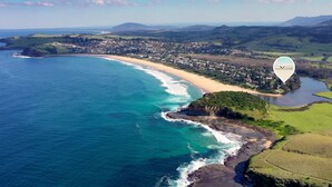 An aerial view of a coastal town with a beach, rocky coastline, and surrounding green fields. - Saltwater - walk to the beach (Werri Beach)