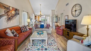 A spacious living room with a sofa, coffee table, and TV. There is a kitchen in the background. - Sprinkle of Irish charm, beautifully updated, Siesta Dunes 8-205 (Siesta Key)