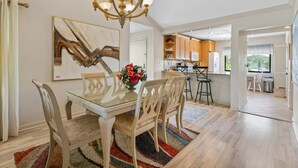 A dining area with a glass table, wooden chairs, a chandelier, and a colorful rug. - Sprinkle of Irish charm, beautifully updated, Siesta Dunes 8-205 (Siesta Key)
