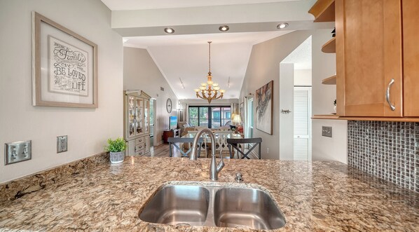 A kitchen with a double sink, granite countertops, and a dining area with a chandelier. - Sprinkle of Irish charm, beautifully updated, Siesta Dunes 8-205 (Siesta Key)