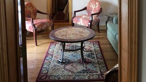 A cozy living room with two floral armchairs, a round coffee table, and a patterned rug. - the Stone Hut (Talkeetna)