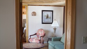 A cozy living room with a round table, a patterned armchair, a sofa, and a framed picture on the wall. - the Stone Hut (Talkeetna)