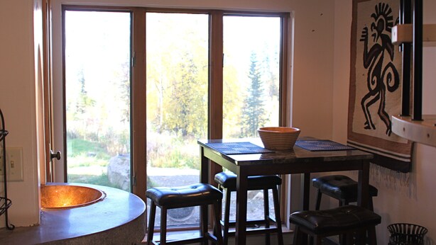 A room with a large window, a round sink, and a table with stools. - the Stone Hut (Talkeetna)