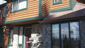 A wooden cabin with stone walls and large windows, featuring a stone fireplace and a view of the mountains. - the Stone Hut (Talkeetna)
