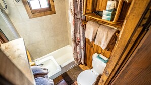 Un baño pequeño y rústico con bañera, inodoro y estantes de madera.