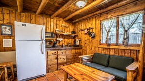 Cocina rústica de cabaña con paredes de madera, un refrigerador blanco, un microondas, un lavamanos y un banco de madera.