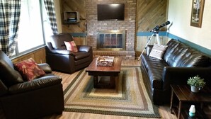 Ein Wohnzimmer mit Kamin, Ledersofas, einem Couchtisch und einem an der Wand befestigten Fernseher.