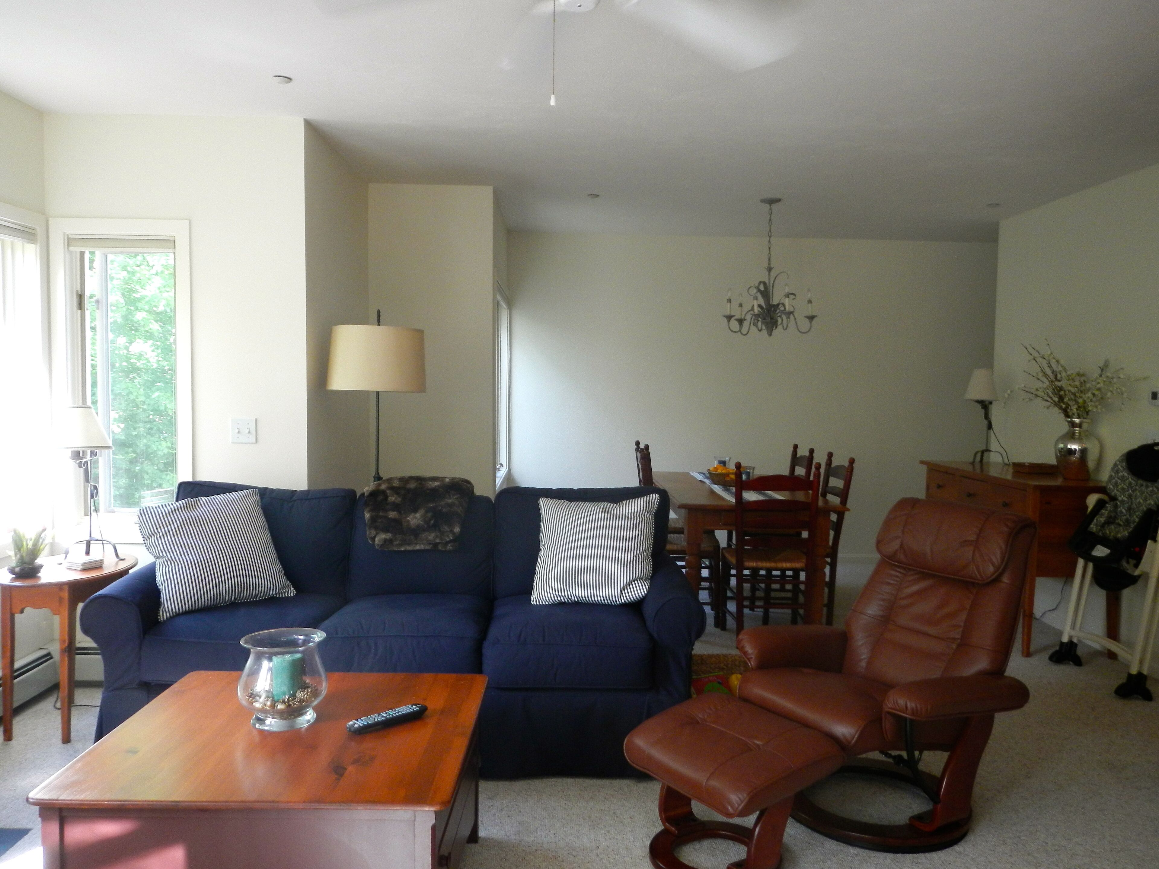 A living room with a blue sofa, a wooden coffee table, a brown leather chair, and a dining area with a table and chairs.