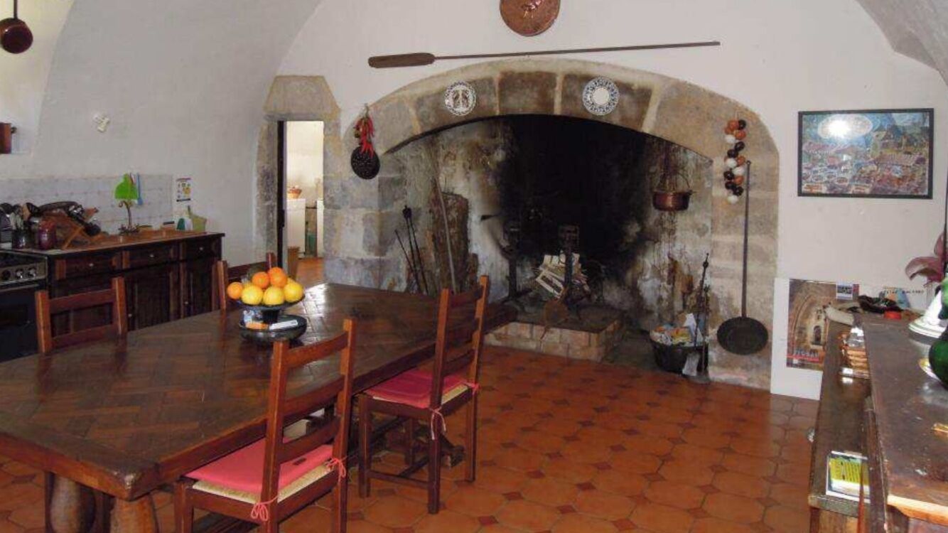 Un coin repas rustique avec une cheminée en pierre, des meubles en bois et un sol carrelé.