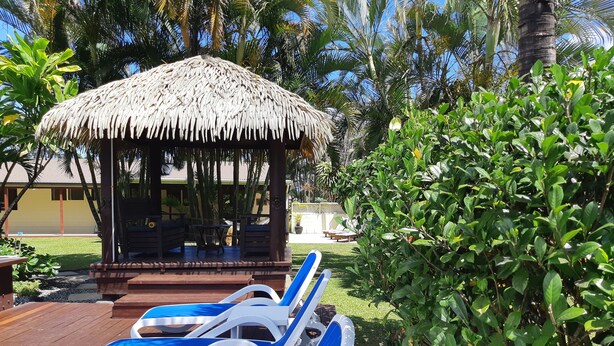 A thatched-roof gazebo with seating, surrounded by lush greenery and a wooden deck with blue lounge chairs. - Island Time Villas - Villa Kakaia (Muri Beach)