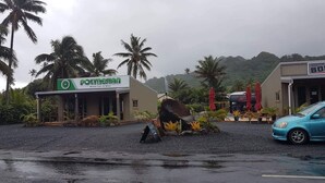 A rental car and bike service center with a signboard, a parked car, and a building with a sign. - Island Time Villas - Villa Kakaia (Muri Beach)