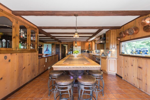 A kitchen with wooden cabinets, a large island with stools, and copper pots on the wall. - Private Pickleball Ct - Indoor Hot Tub - Spa Room - Lift Tkts (Windham)