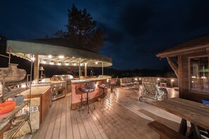 Een buitengebied met een bar, een overdekte zithoek, een barbecue en een houten terras.