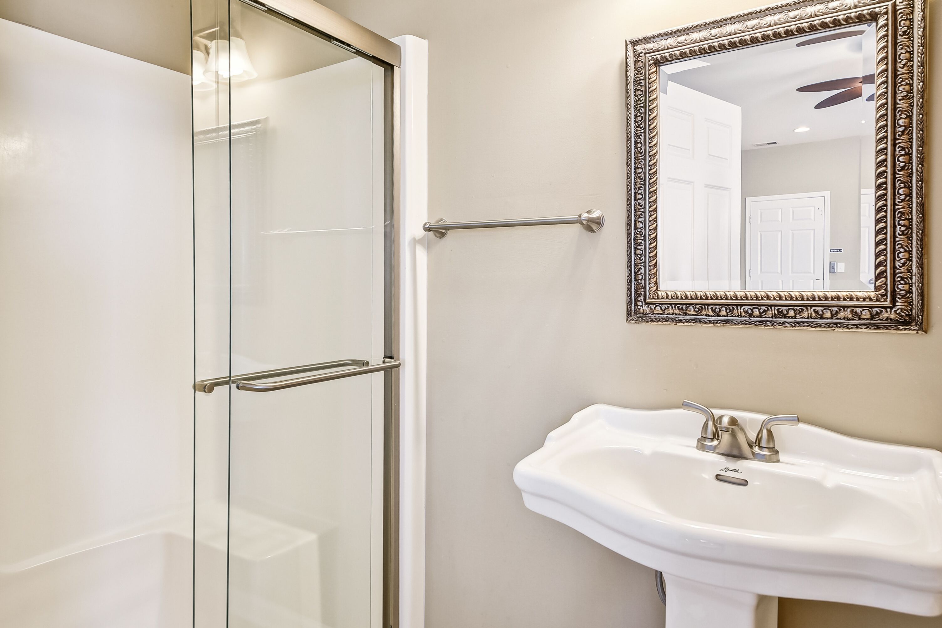 Un bagno con box doccia in vetro, lavabo bianco e uno specchio con cornice decorata.