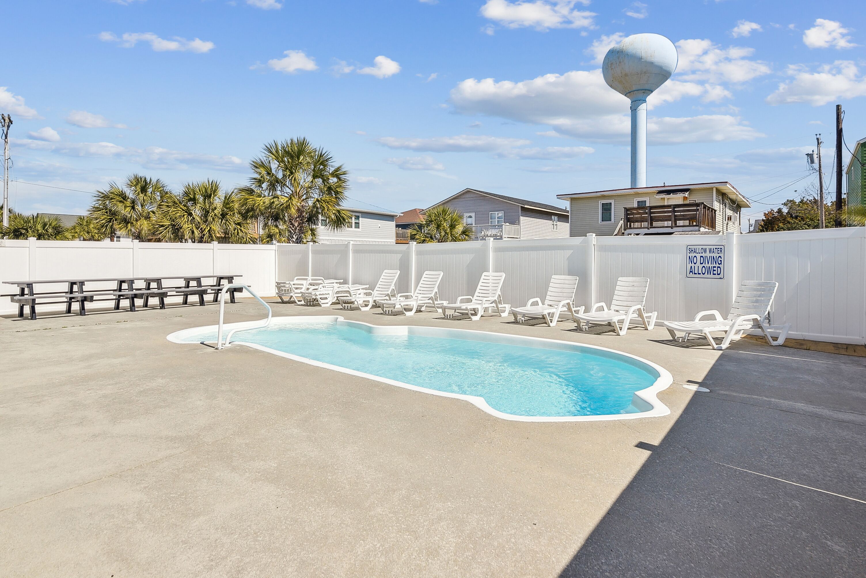A swimming pool with lounge chairs and a sign indicating shallow water and no diving allowed.