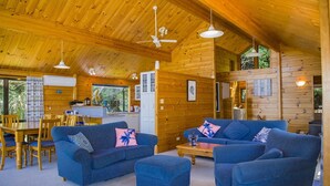 A cabin interior with wooden walls and ceilings, a dining area with a table and chairs, and a living room with a sofa and ottoman.