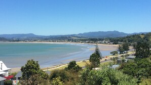 A coastal landscape with a beach, houses, and mountains in the background.