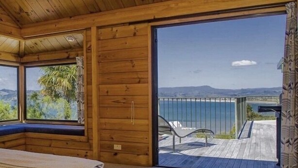 A wooden cabin with a large sliding glass door leading to a balcony with a view of the sea.