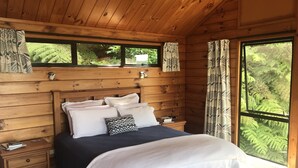 A wooden cabin bedroom with a bed, nightstands, and a window with curtains.