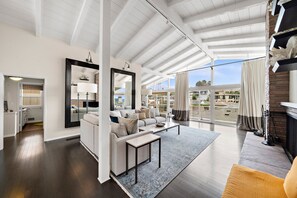 A spacious living room with a high ceiling, a large window, and a view of the cityscape.