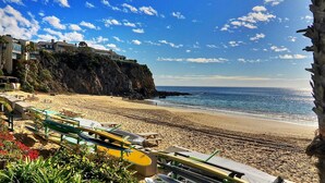 Una spiaggia con una scogliera rocciosa, una fila di edifici e diverse kayak disposti sulla sabbia.