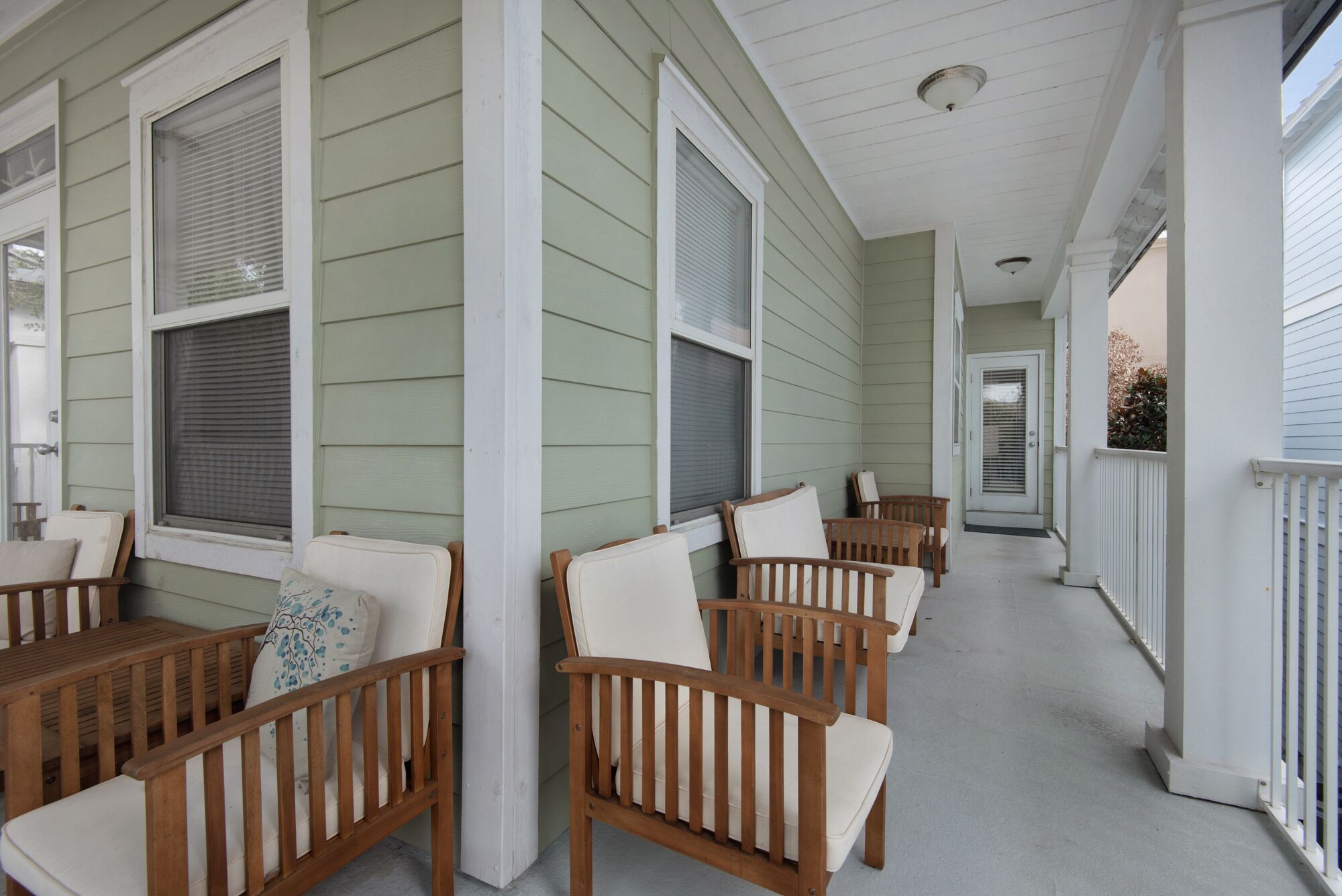 A covered porch with wooden chairs and a bench, featuring a light green exterior and white trim.