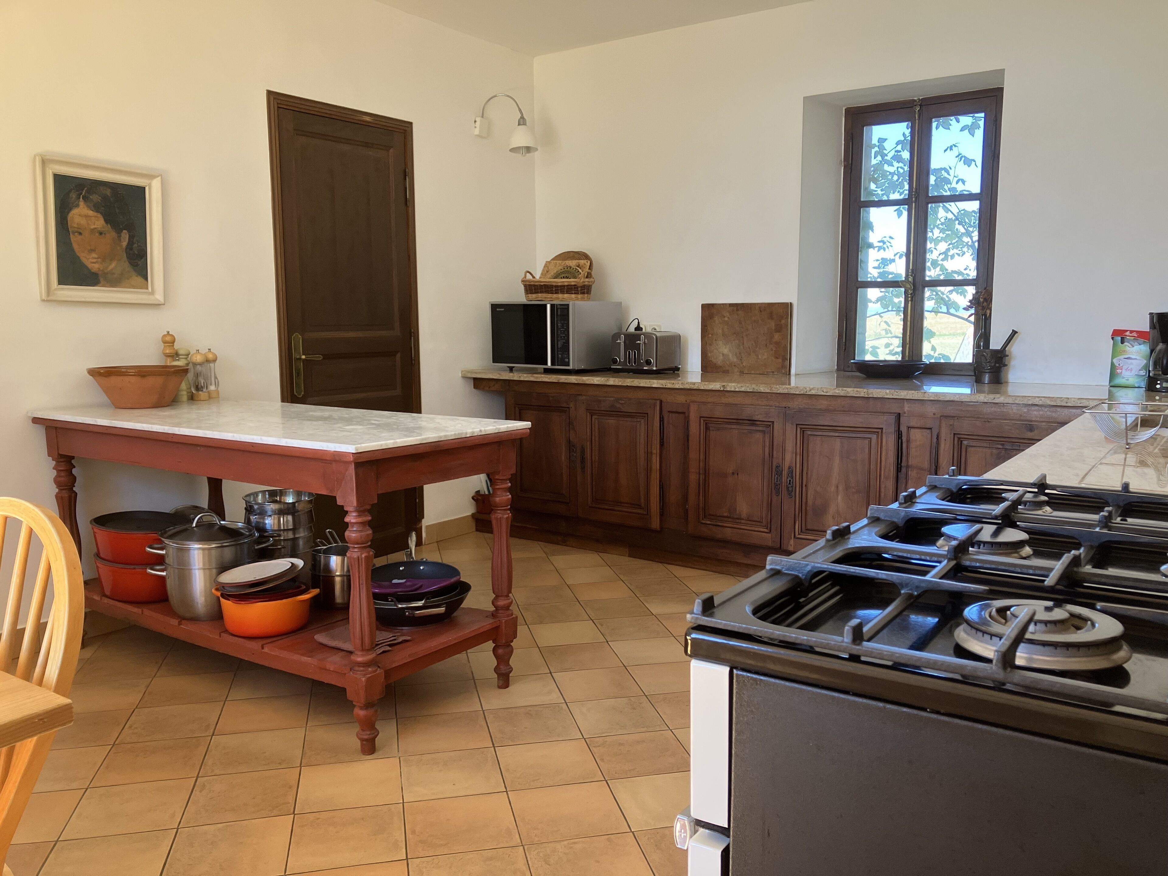 A kitchen with a wooden table, cabinets, a stove, and a window.