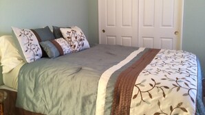 Um quarto com uma cama, almofadas, uma porta e duas imagens emolduradas na parede.