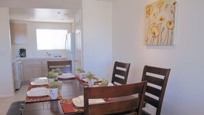 Uma área de refeições com mesa de madeira posta para quatro pessoas, cadeiras e um quadro na parede.