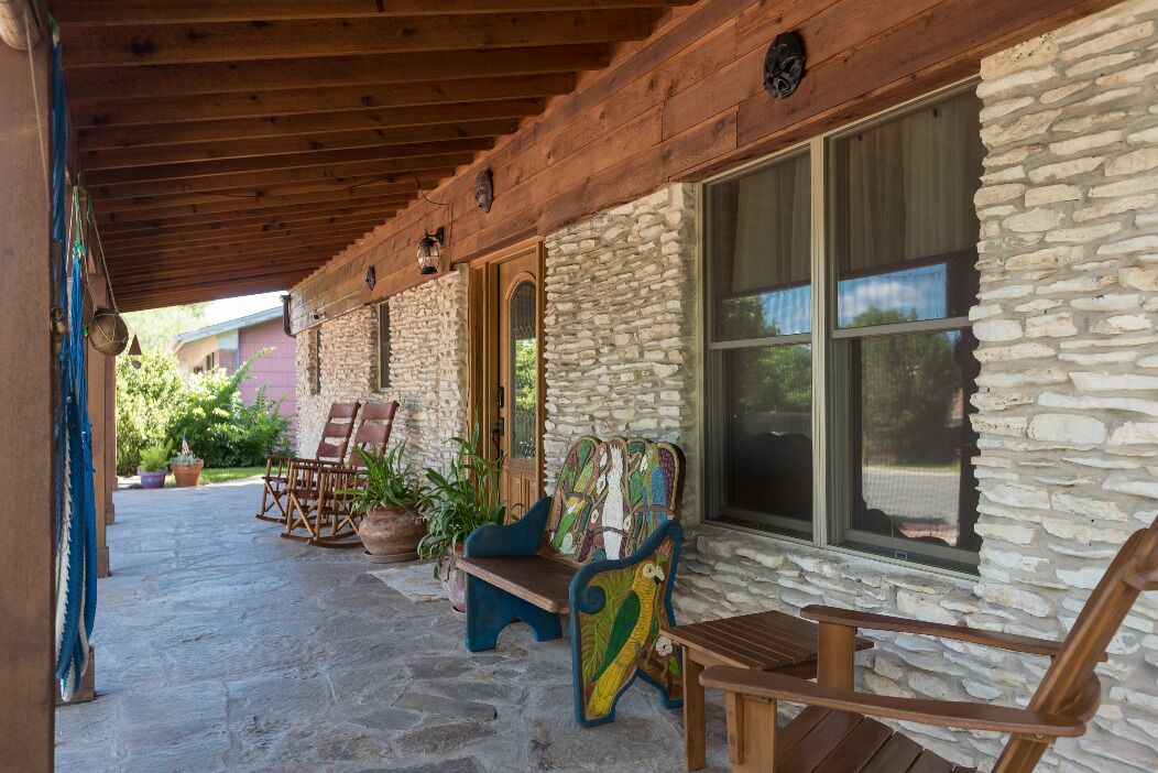 A covered patio with stone walls, wooden furniture, and potted plants.