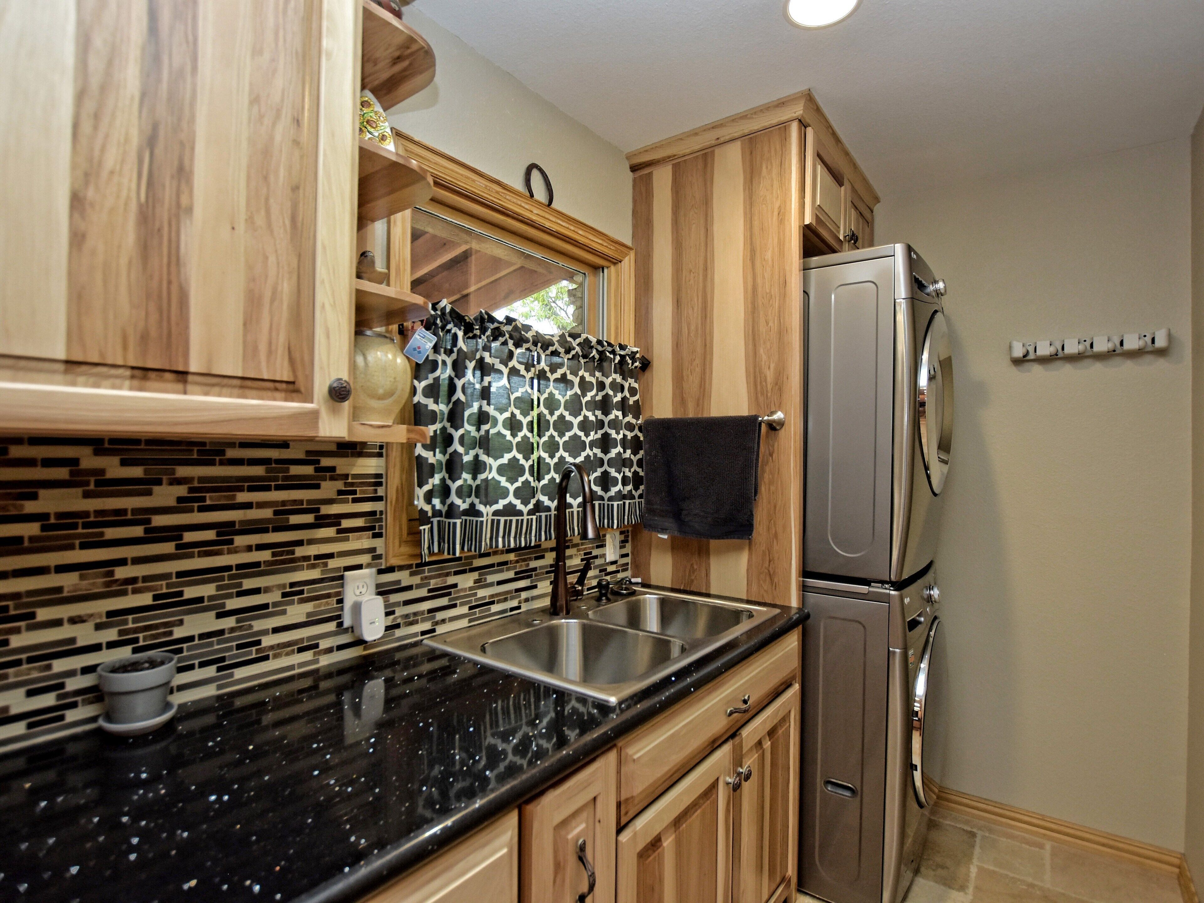 A kitchen with wooden cabinets, a black granite countertop, a stainless steel refrigerator, and a patterned backsplash.